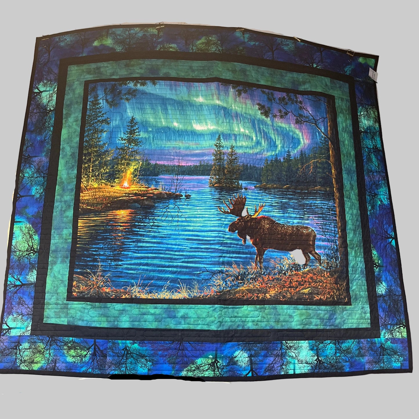 Quilt with a moose and northern lights design in a forest setting.