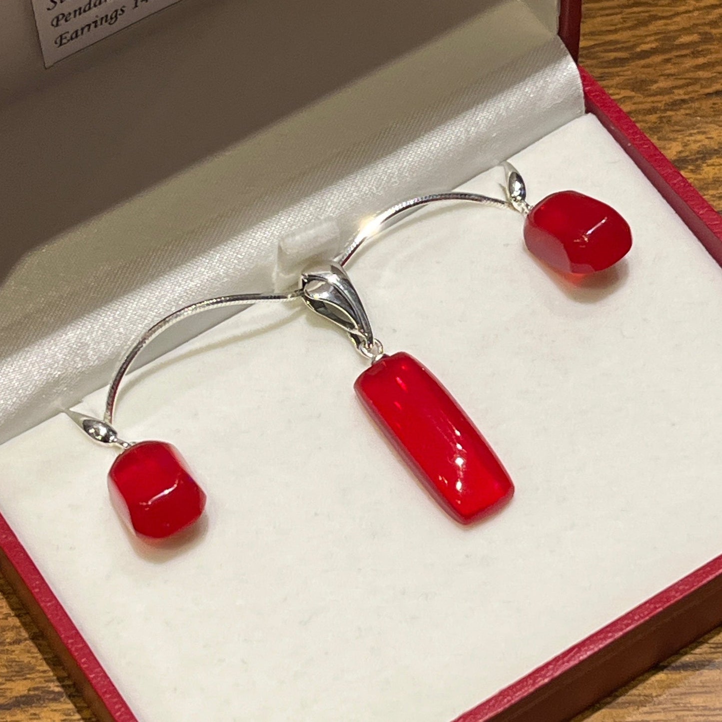 A set of sterling silver jewelry including a necklace and earrings with red fire opal pendants and earrings, presented in a rec and white case. Mexican Red Fire Opal necklace and earring set in sterling silver.  Pendant: 10.45 ct  Earrings: 14.67 ctw. Certified Made in Alaska and Silver Hand jewelry. This unique piece is authentic Alaska Native art created by an enrolled member of an Alaska Native tribe. 